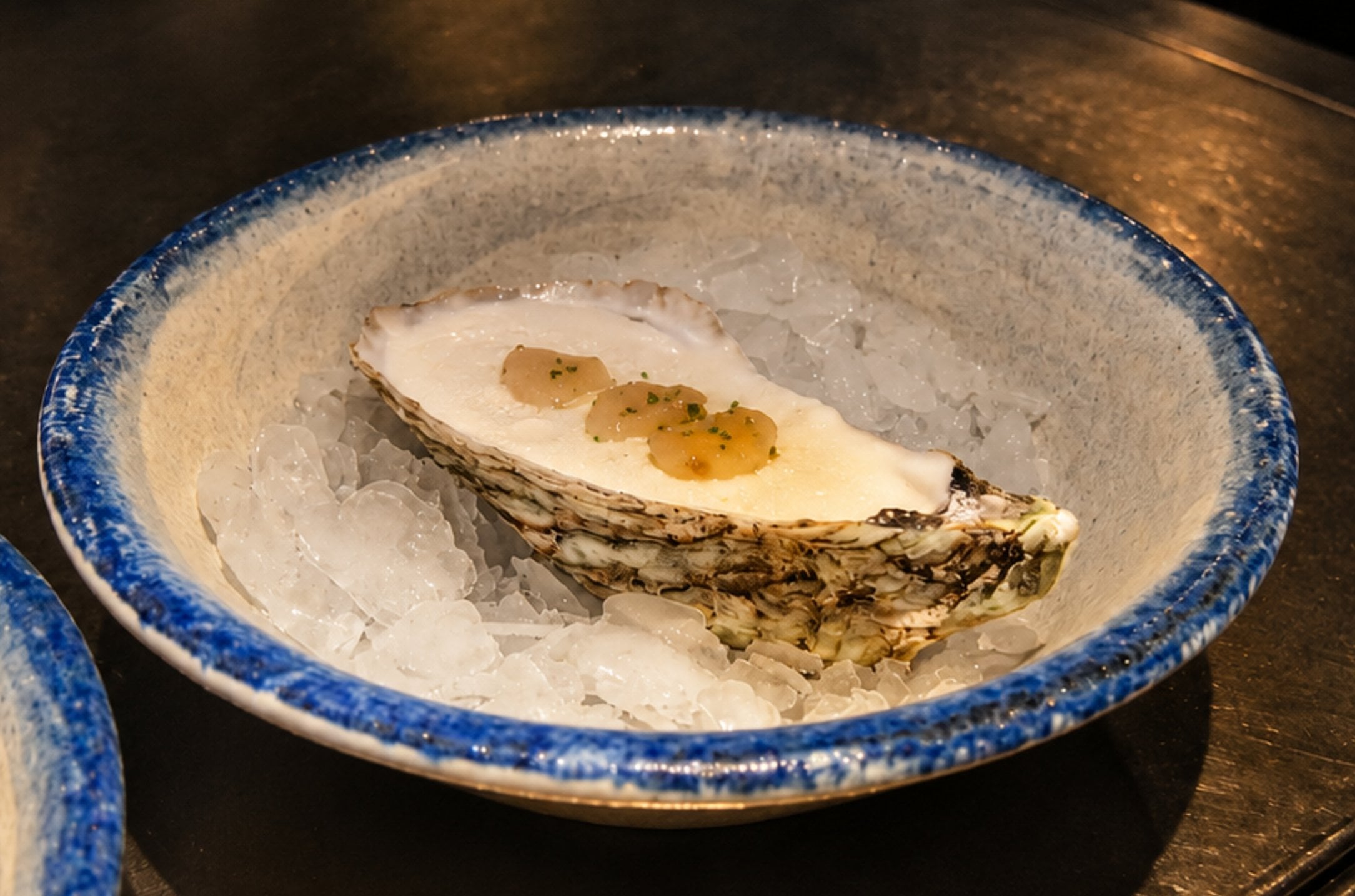 Fresh oyster with a citrus pearl topping in a ceramic bowl on ice